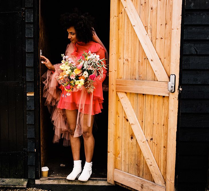 Stylish bride in a short red wedding dress with white bridal boots and a long pink veil 