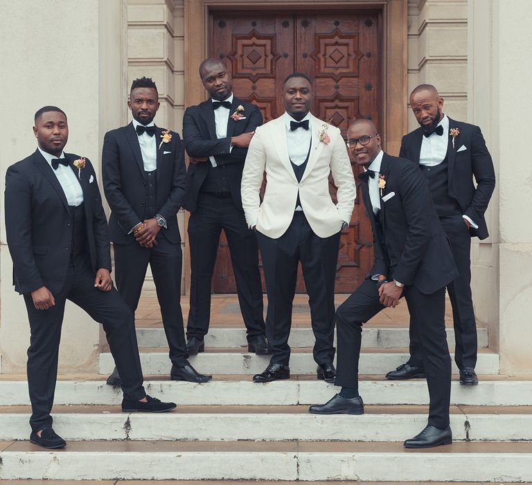 Groom stands on staircase with ushers on his wedding day