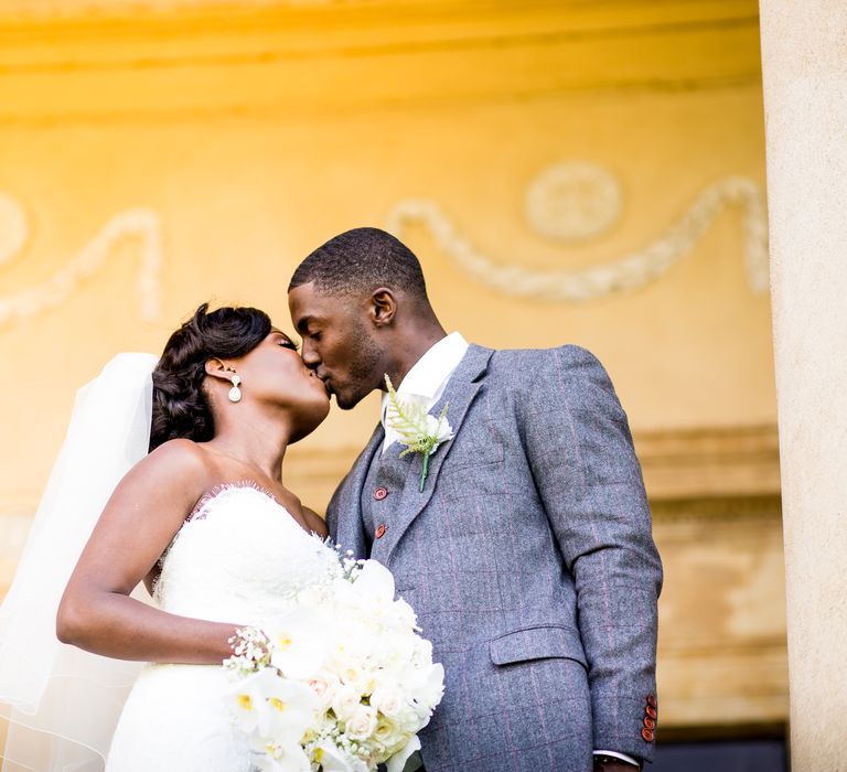 Bride & groom kiss on their wedding day as groom wears pale blue suit