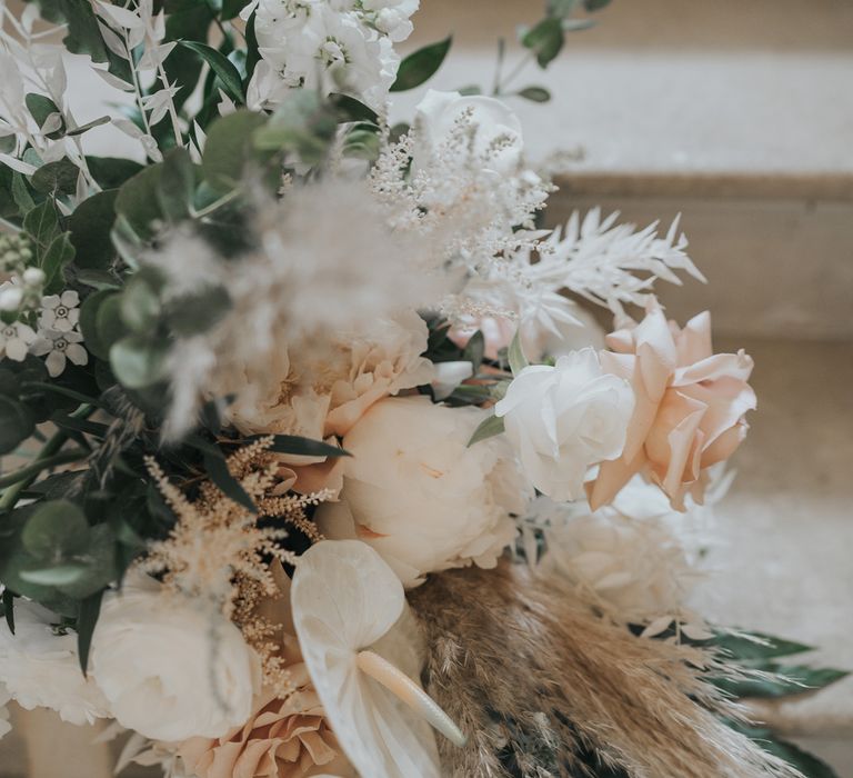 White and blush pink rose wedding bouquet with green foliage and pampas grass on stone steps at Came House Dorset Wedding