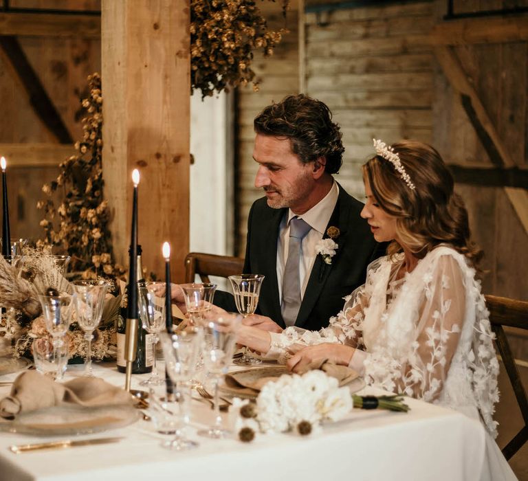 Bride and groom sat inside rustic barn at High Billinghurst Farm at a neutral luxe tablescape