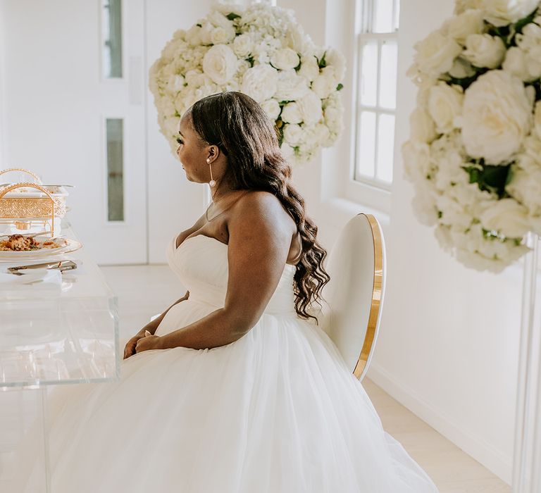 Bride sits down at reception venue as her wedding gown fans out around her