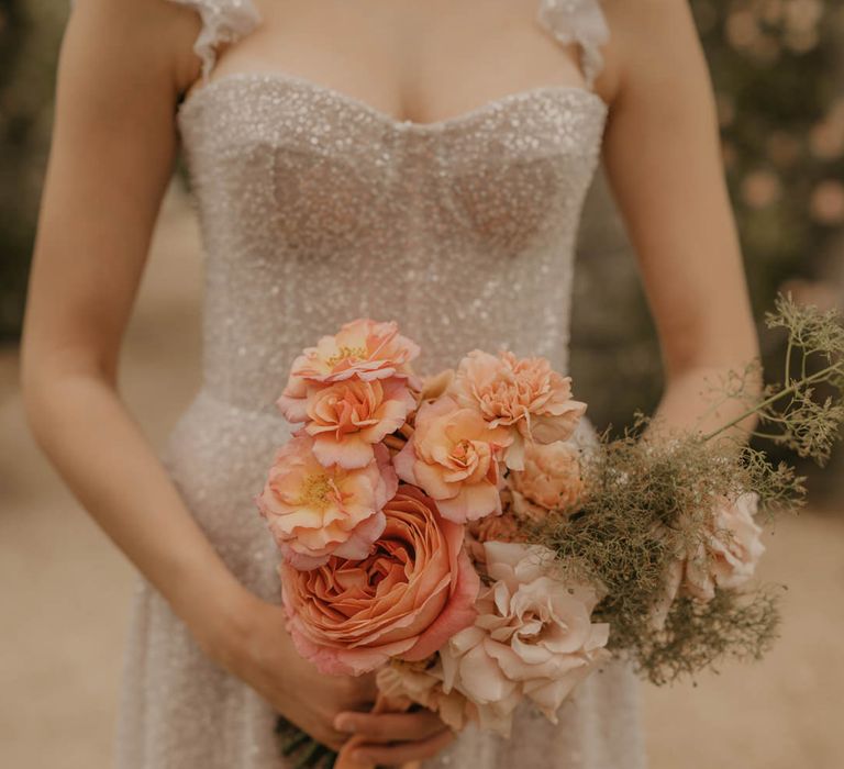 Bride in a sparkly Made With Love dress holding an orange, coral and peach wedding bouquet 