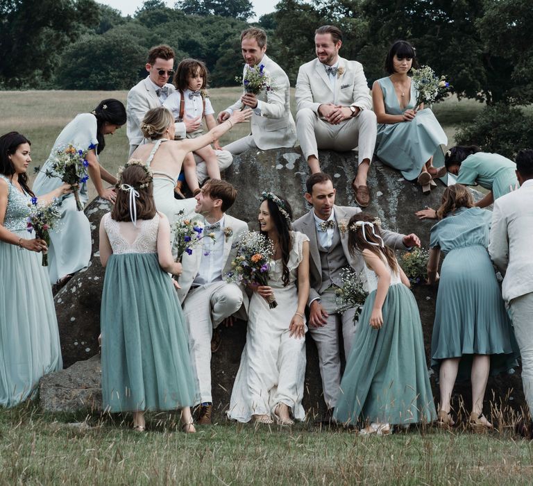 Bride & groom sit with their wedding party for post-wedding pictures as Groomsmen wear light coloured suits and bridesmaids wear different shades of green