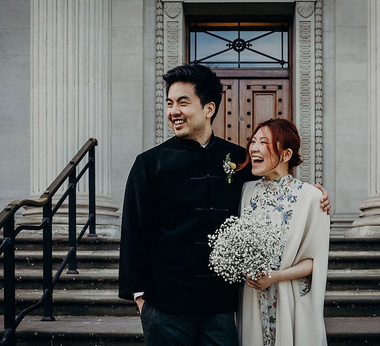 East Asian bride and groom standing outside the resisgty office at their micro wedding smiling and holding a gypsophila wedding bouquet 