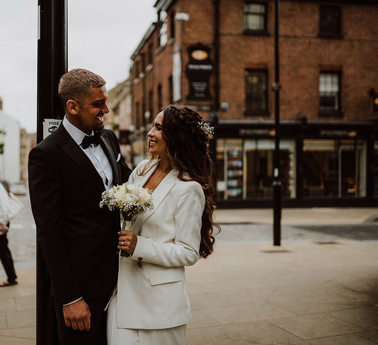 Groom in black tuxedo from Reiss smiling at his bride in a white suit at their Sheffield Registry Office wedding 