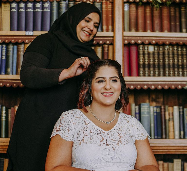 Indian bride in lace wedding dress having her hair done in the library at Dulwich College 