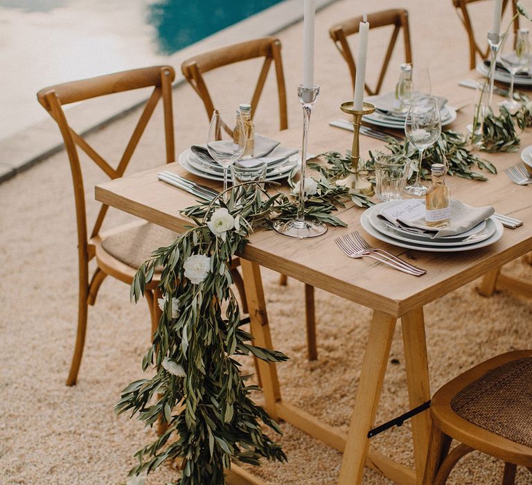 Olive branch table runner hangs off wooden table with rustic vibe complete with delicate white flowers 