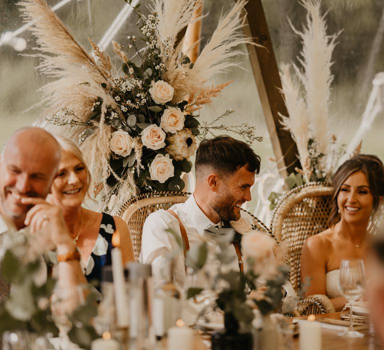 Bride & groom laugh during reception surrounded by pampas grass and sitting in wicker chairs | Mark Bamforth Photography