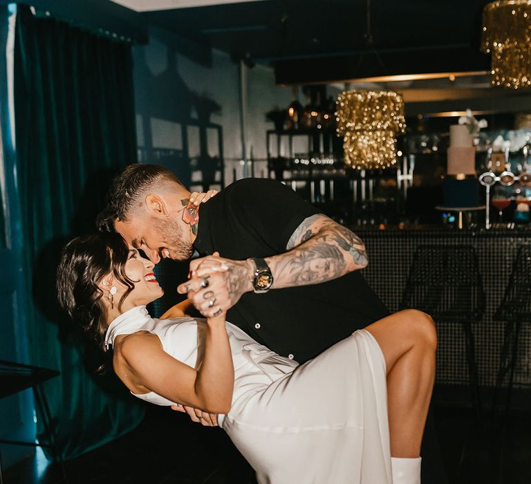 Groom with tattoos in a short sleeve black shirt leaning his bride over on the dance floor revealing her white boots 