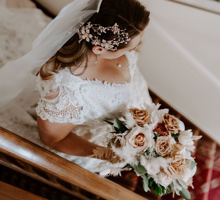 Bride in handmade wedding dress, veil and intricate bridal headpiece walks downs stairs holding mixed rose bridal bouquet before DIY garden wedding in Bedfordshire