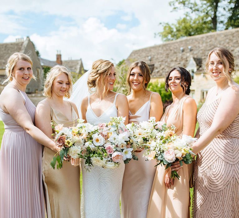 Bridal party in different blush, baby and vintage pink bridesmaid dresses holding white and pink flower bouquets 