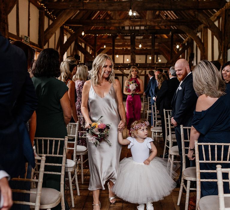 Flower girl in a tulle skirt, trainers and flower crown walking down the aisle 