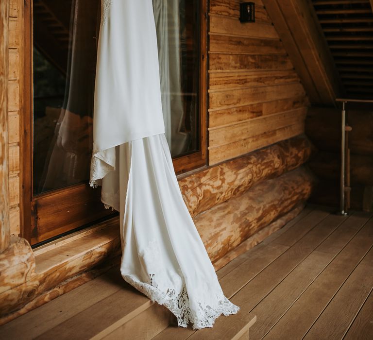 Lace wedding dress with train hanging in barn for rustic Lake District wedding