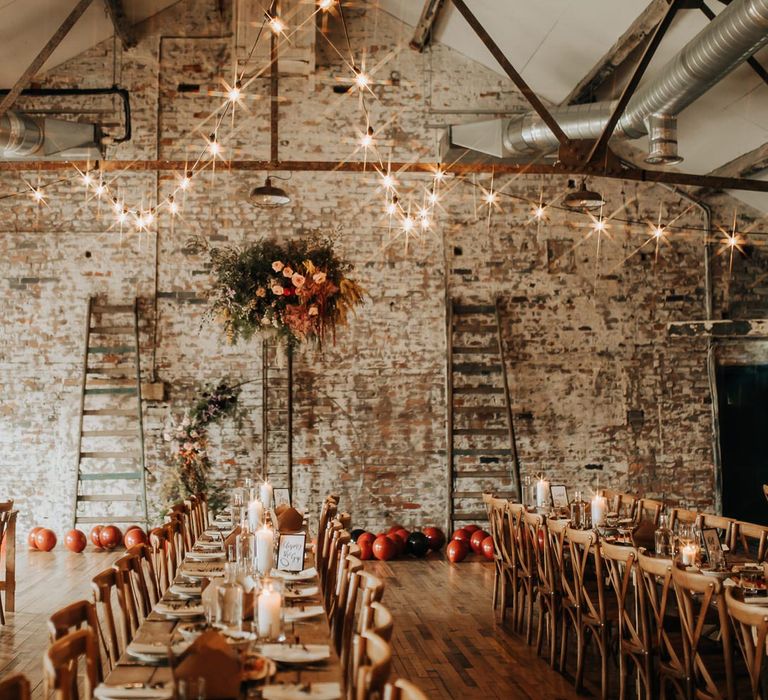 Interior of wedding reception room at Scale wedding venue in Liverpool with exposed brick, long wooden wedding table, flower cloud and bulb string lights