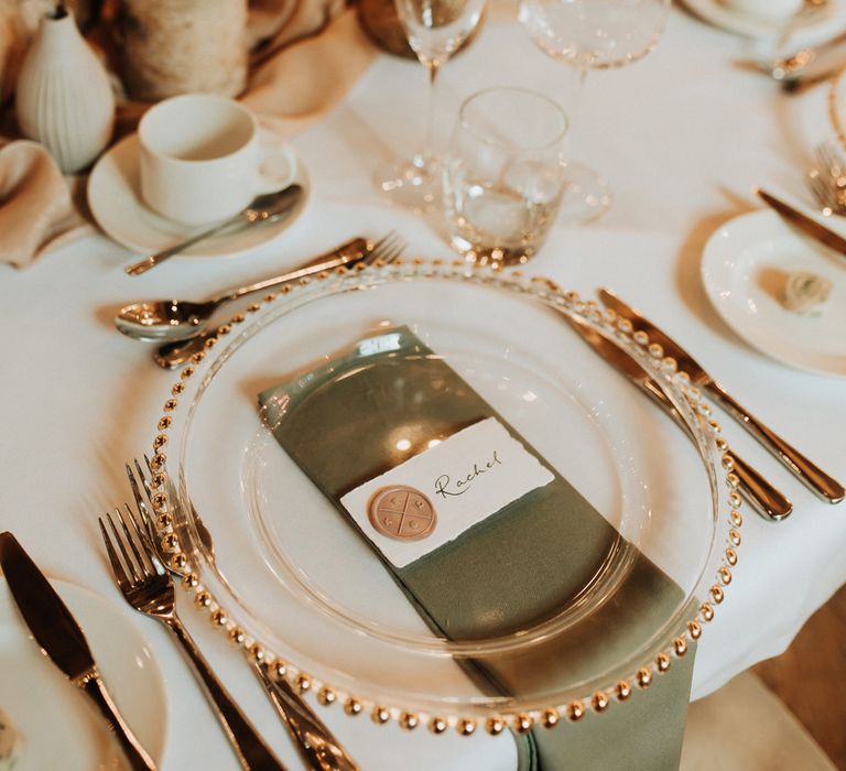 Clear plate with gold trim, caligraphy table place names and green napkins for chic wedding table setting