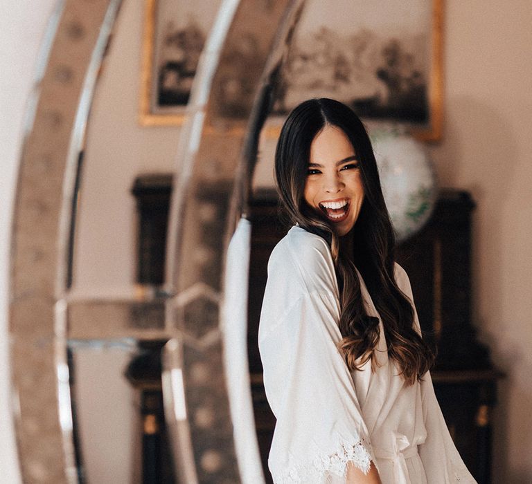 Bride with long brown wavy hair wearing a satin getting ready robe on her wedding morning 