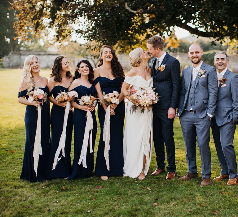 Bride and groom with their bridesmaids in navy blue dresses and groomsman in pale grey blue at country house wedding