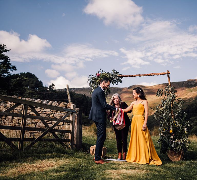 Outdoor wedding with handfasting ceremony and bride in a yellow wedding dress