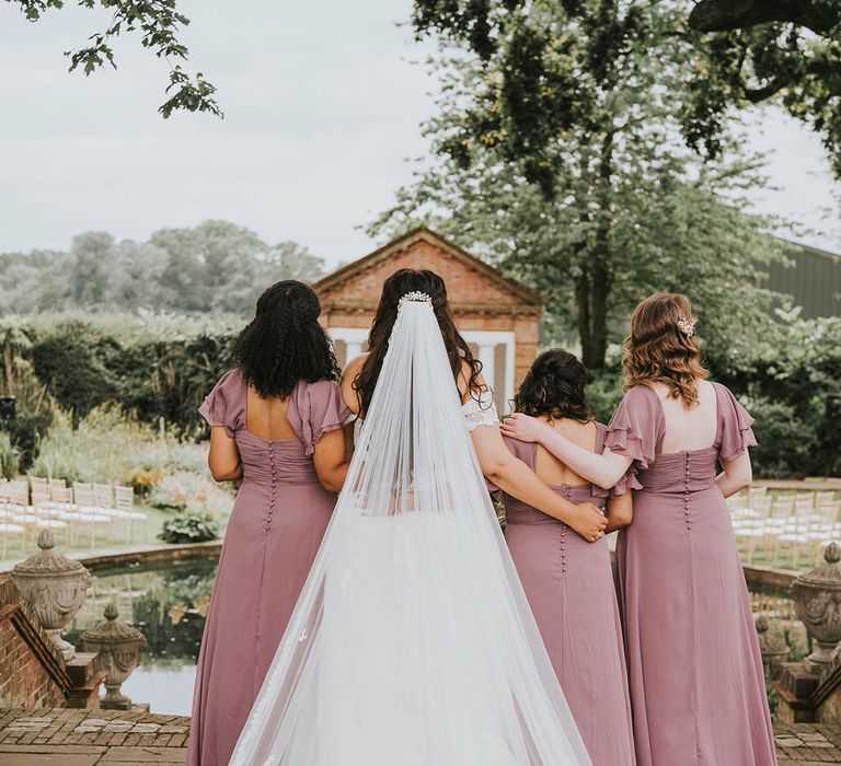 Vintage pink bridesmaid dresses with button detail and bride in off the shoulder white lace dress with lace veil for outdoor wedding