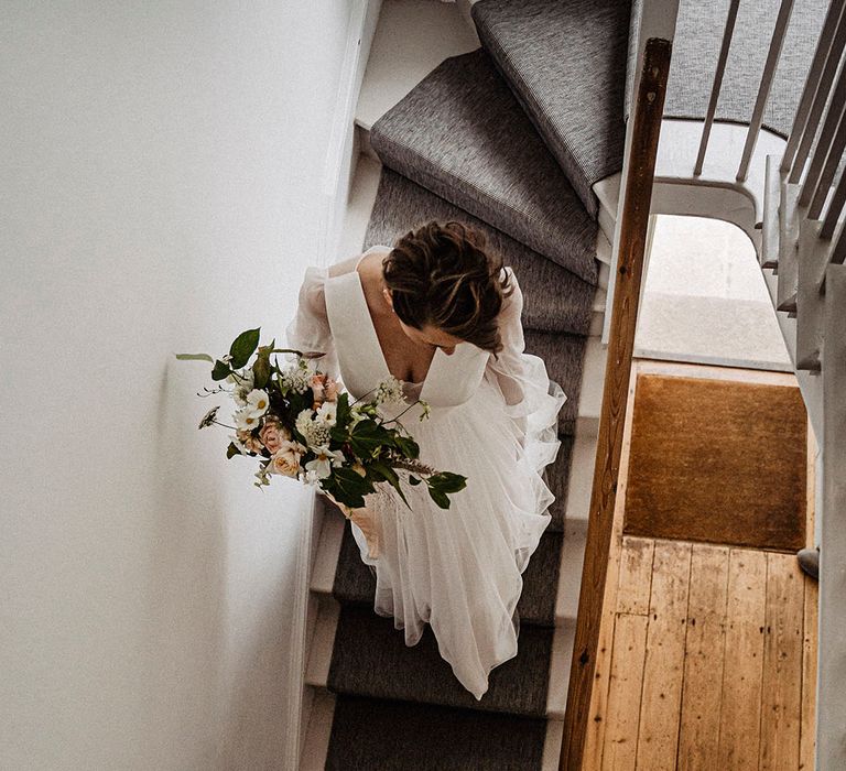 Bride carrying pink rose and dahlia bouquet with white cosmos flowers as she descends the stairs with the groom