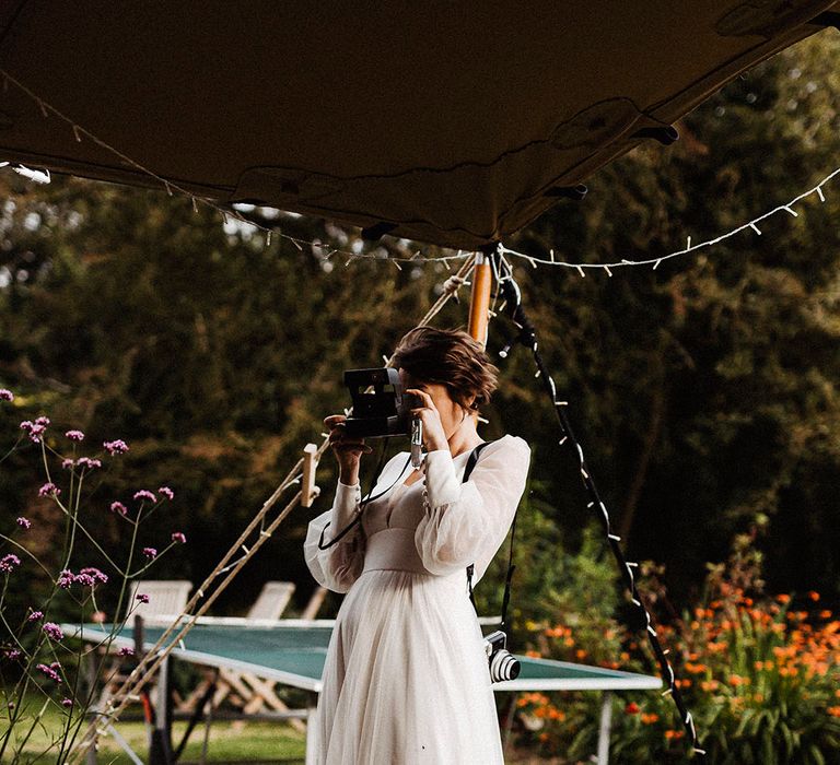 Bride takes her own pictures on her wedding day wearing sheer long sleeve gown with button detail