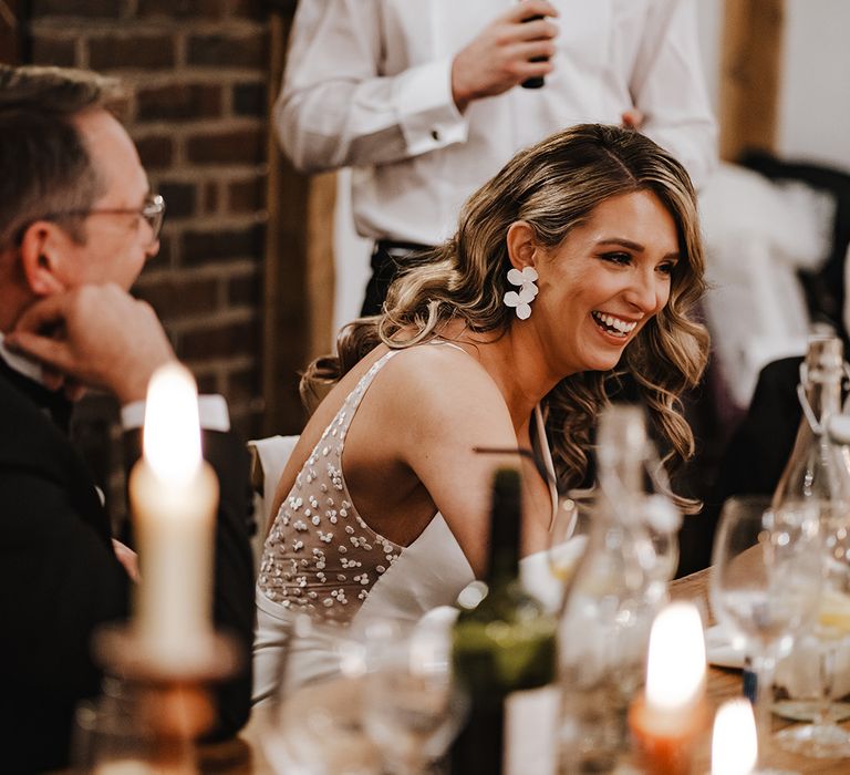 Bride wearing white flower earrings laughs at the groom's speech with black bow tie