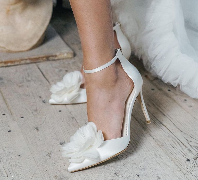 White stiletto wedding shoes with white flower and ankle strap worn by bride with ruffle wedding dress 