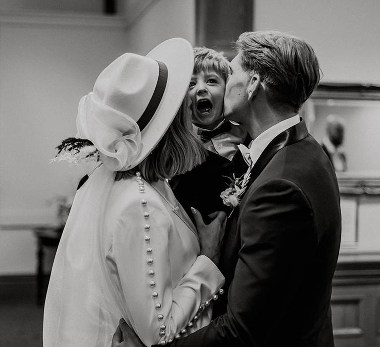 Bride and groom kiss little boy on either cheek in black tie for town hall wedding 