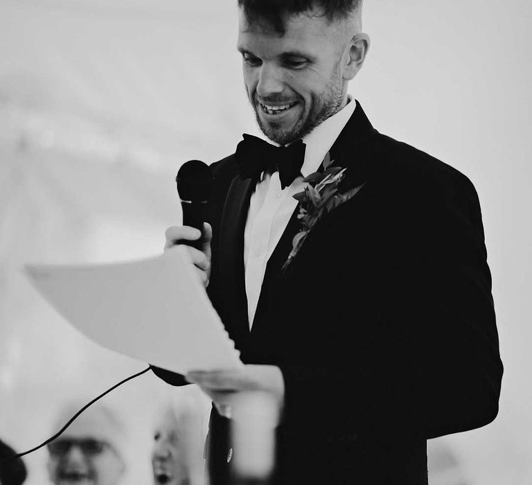 Groom in black tie reads out his wedding speech 