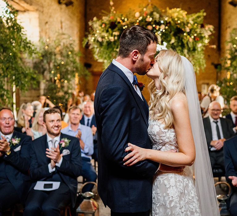 Bride and groom share their first kiss as a married couple at the Cripps Barn wedding venue with greenery 