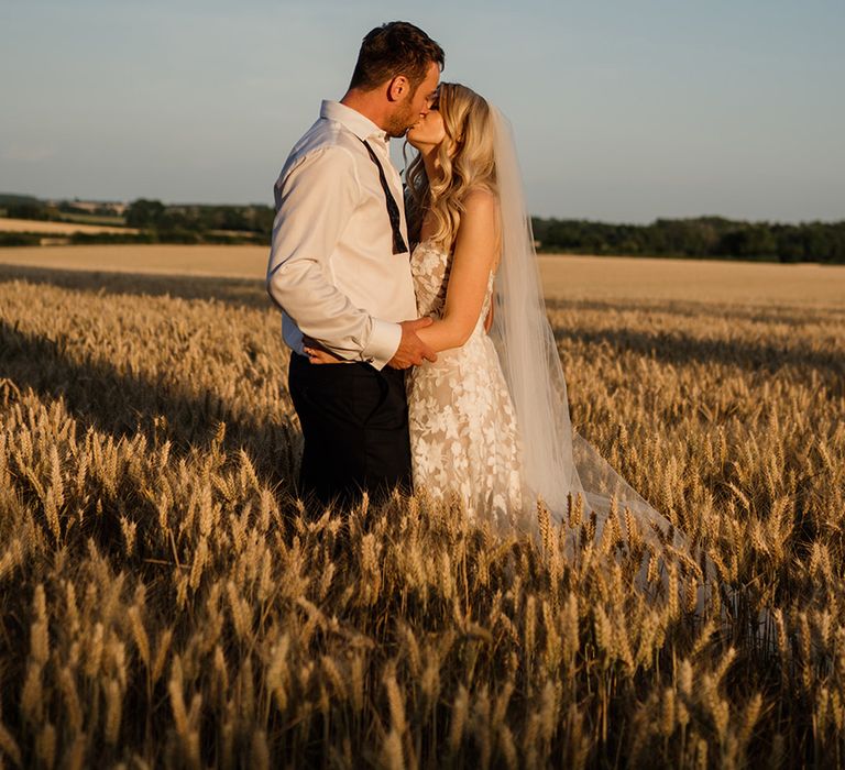 Bride and from share a kiss in a field with bride in Lillian West wedding dress 