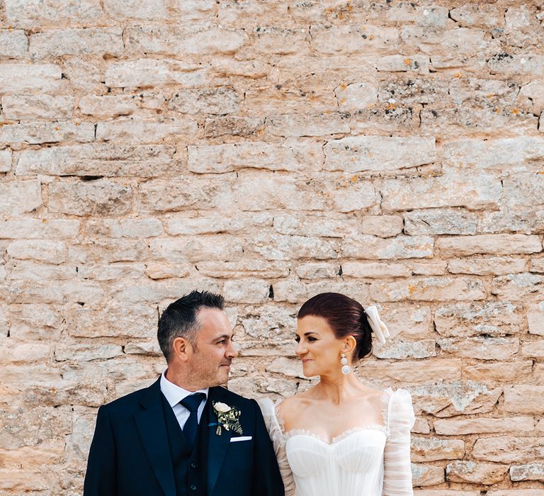 Groom in blue suit and bride in ruffle tulle princess wedding dress look at each other with bride wearing a white bow in her red hair 