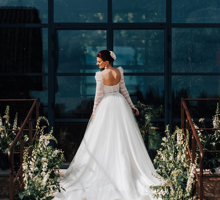 Bride in Emma Beaumont wedding dress with detachable ruffle sleeves and princess skirt with white hair bow and white flower decor 