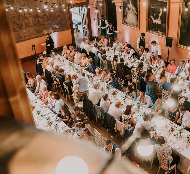 Guests sit at banquet tables with white tablecloths and lights hanging above for Cowdray House reception 