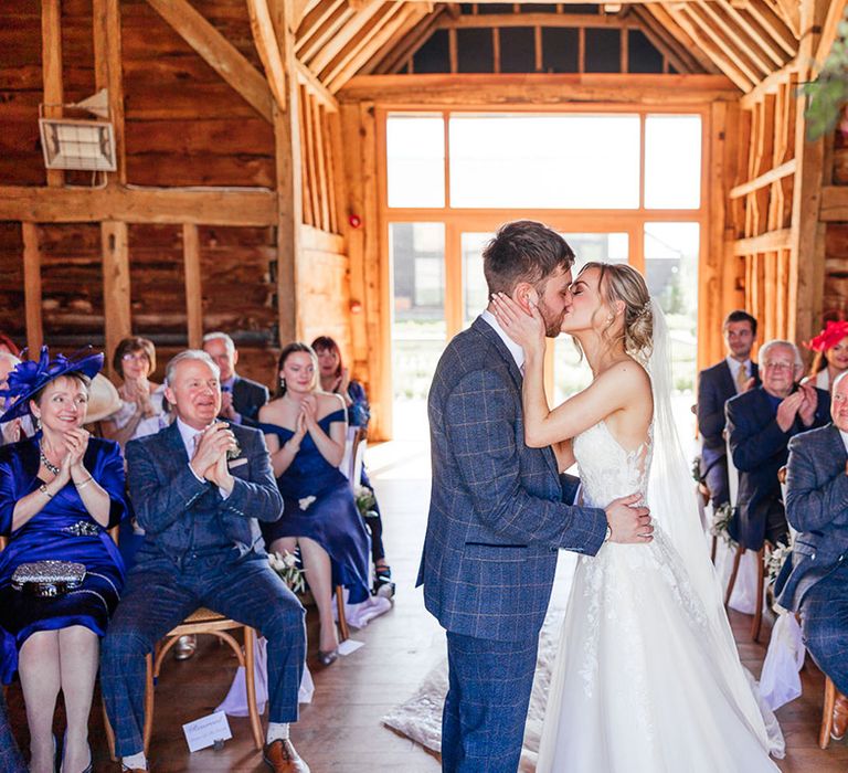 Bride and groom share their first kiss as a married couple with wedding guests in pink and blue 