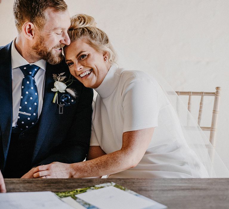 Bride smiles and leans into the from as they sign their register 