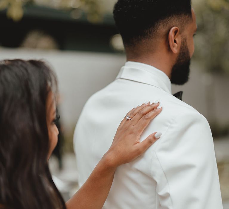 Bride places her hand on grooms shoulder during first-look moment outdoors 