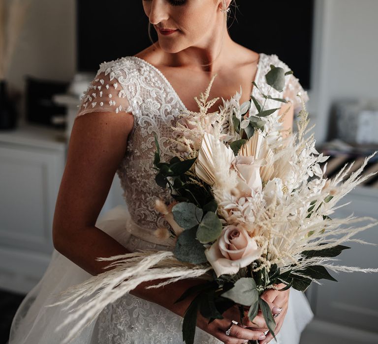 Bride wears capped sleeve wedding gown and holds pampas grass bouquet 