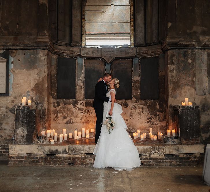 Bride & groom kiss in front of pillar candles at The Asylum on their wedding day