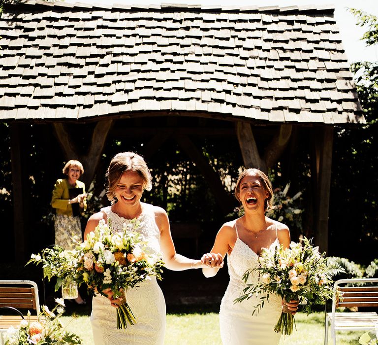 Brides with intertwined fingers walk back down the aisle as a married couple 