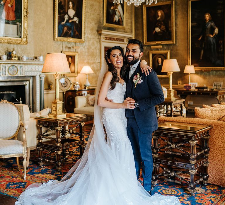 Bride wearing fitted lace wedding dress & groom laugh in grand room at Syon Park 