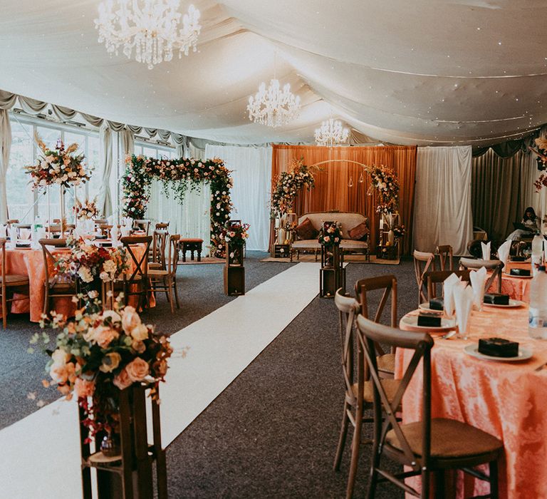 Chandeliers hang above Autumnal styled room complete with floral centrepieces and floral archways 