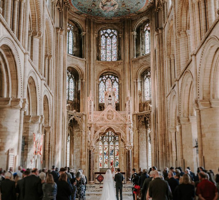 The bride and groom stand at the altar and the guests are seated at Peterborough Cathedral 