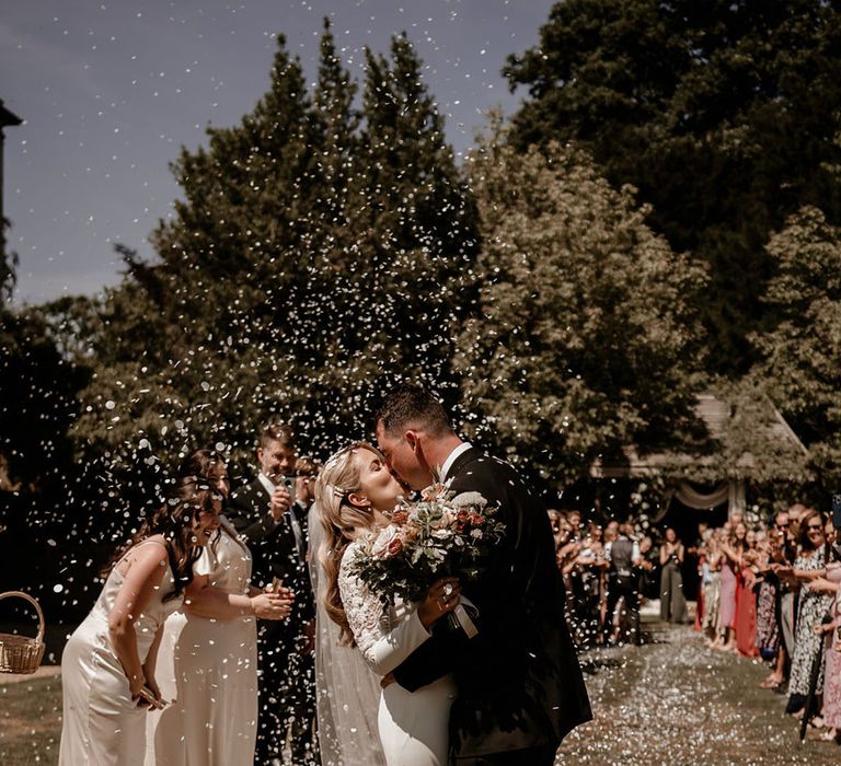 Bride in a long sleeve fitted wedding dress from Badgley Mischka kissing the groom for their outdoor wedding ceremony 