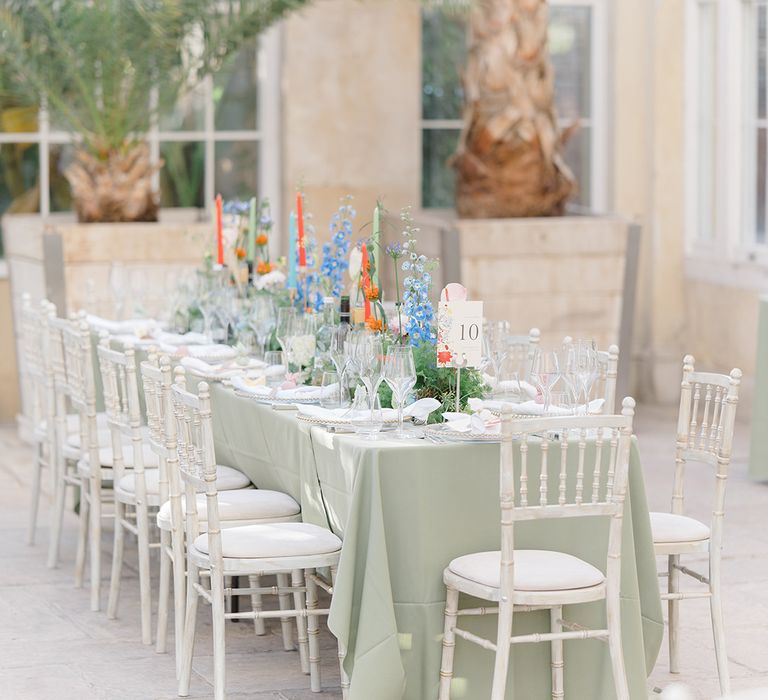 Pastel toned wedding reception at Syon Park with pale green tablecloths, brightly coloured floral arrangements lining the table and white chairs 