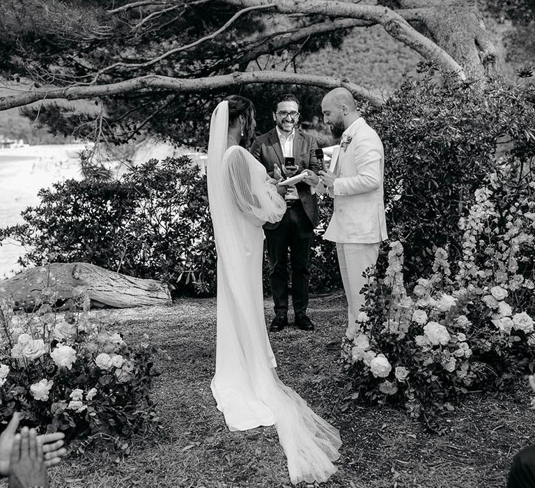 Bride and Groom together at the alter surrounded by flowers trees and sea at Torre de Bosis wedding venue in Portonovo, Italy