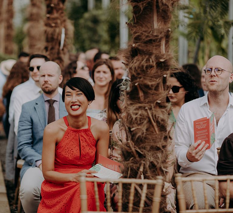 Guest in bright red halter-neck dress smiling during ceremony