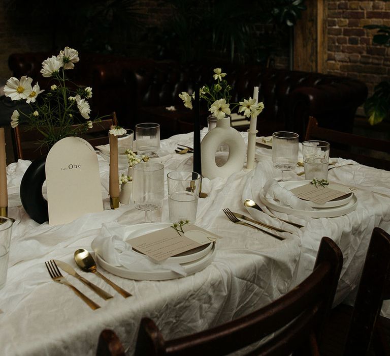 Monochrome wedding tablescape at 100 Barrington with rounded off white table numbers, gold cutlery, black and white table decorations and vases, and white floral arrangements