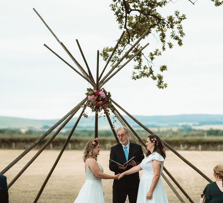 Brides participate in their outdoor wedding ceremony for their lesbian wedding with flower crowns and wooden boho altar decoration 